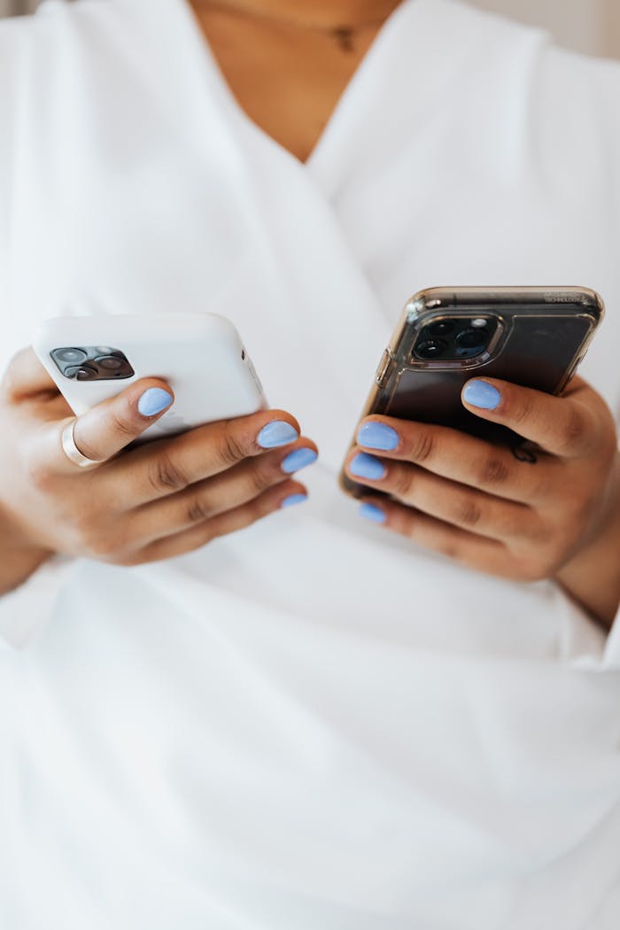 Close-up of hands with blue nails holding two smartphones, showcasing modern technology.
